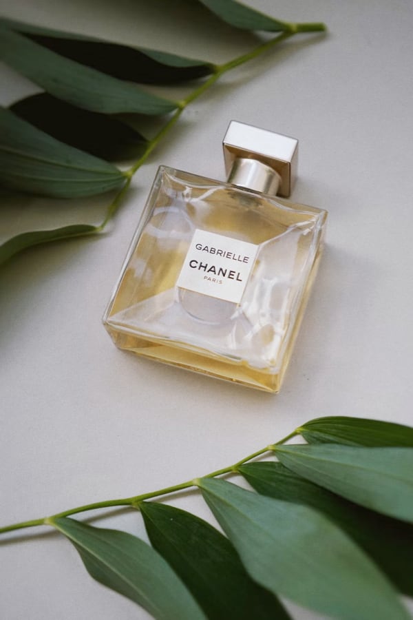 Gabrielle Essence Eau De Parfum bottle lying on a flat surface with green leaves decorating around it